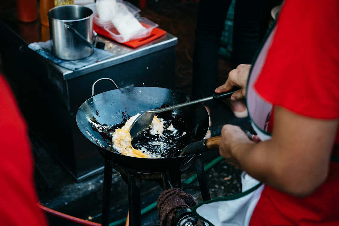 A vendor preparing pad thai in a large wok on Yaowarat Road at night, with flames rising from the pan