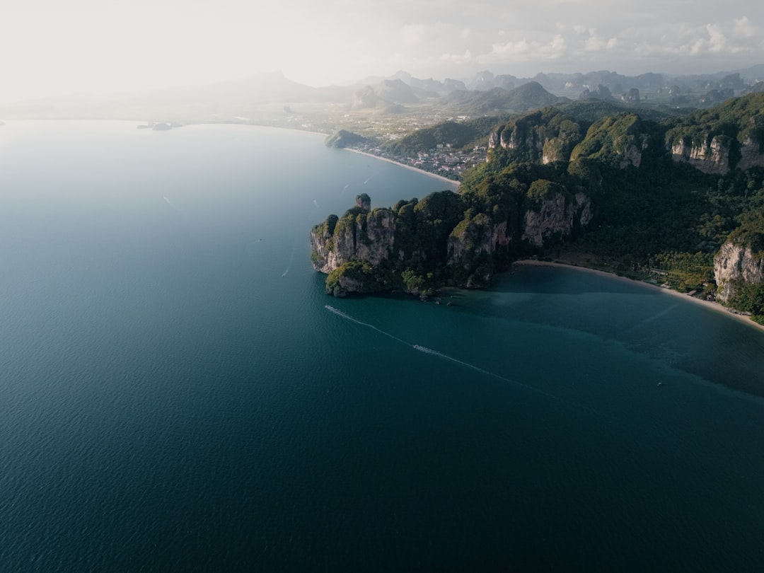 Climber on a limestone cliff at Railay Beach with the Andaman Sea and longtail boats visible below