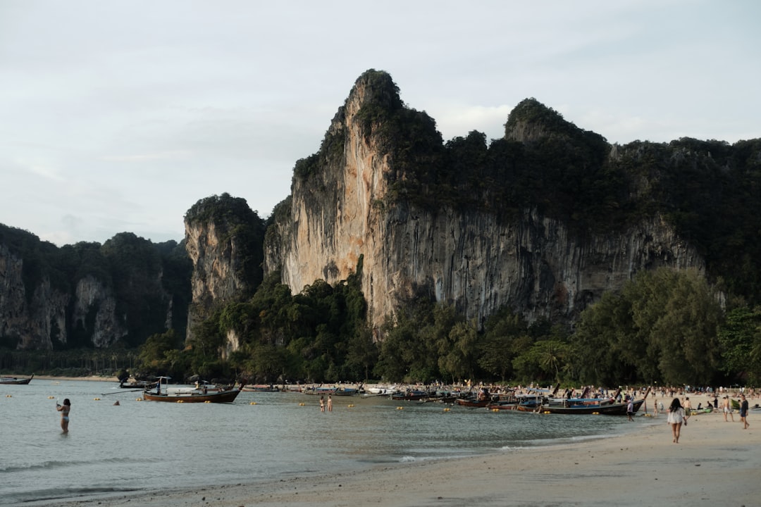 Longtail boats lined up on Railay West Beach with dramatic limestone cliffs in the background